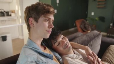 Young mixed race gay couple cuddling on the couch spending quality time together watching movie at home