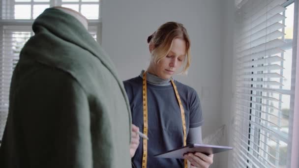 Caucasian focused female designer designing coat for women writing in digital tablet for measurements — Stockvideo