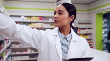 Mixed race female pharmacist searching through isles of pharmacy checking on digital tablet