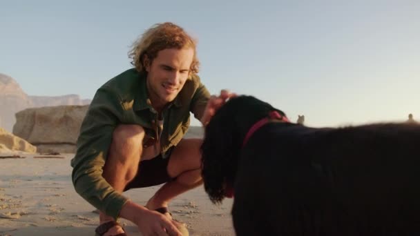 Un joven macho caucásico jugando pelota con perro feliz en la playa durante el atardecer. Hombre mirando a su perro. Imágenes de alta calidad 4k — Vídeos de Stock
