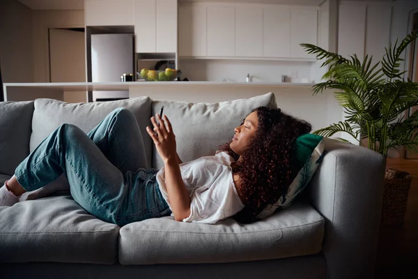 Gemengde race vrouwelijke student ontspannen op de bank sms 'en op cellulaire apparaat — Stockfoto