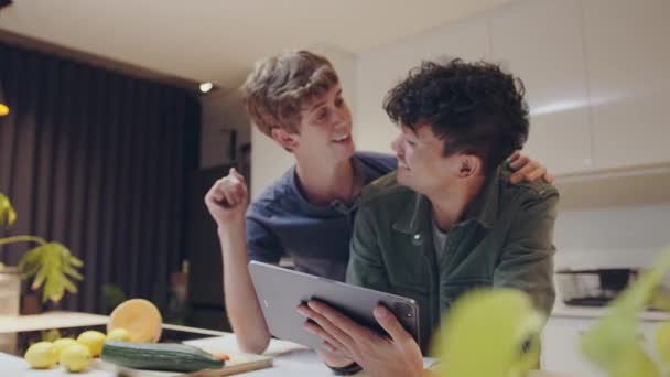 Feliz casal masculino colagem segurando tablet digital sorrindo e rindo na cozinha — Vídeo de Stock