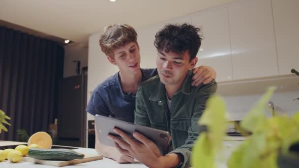 Mixed race male couple bonding in kitchen searching recipes on digital tablet for dinner — ストック動画