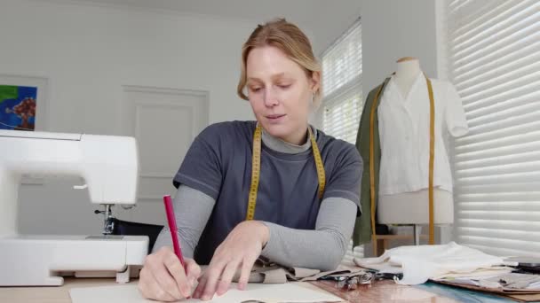 Běloška žena módní návrhářka psaní poznámek v notepadu, zatímco sedí za stolem — Stock video