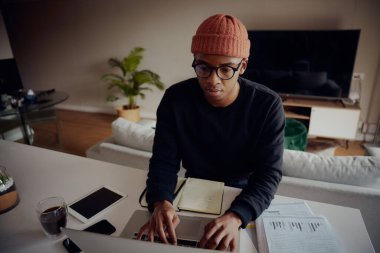 Evden çalışan ve bilgisayarını karıştıran Afro-Amerikan erkek. Afrikalı Amerikalı bir adam dizüstü bilgisayarında notlar yazıyor. Yüksek kalite fotoğraf