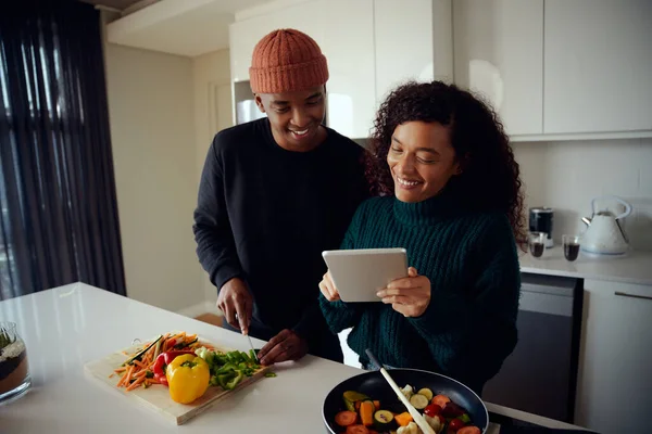 Young mixed race couple cooking food in the kitchen and using a tablet. Woman looking at tablet for food recipe. High quality photo — Stock Photo, Image