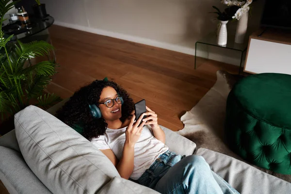 Estudante do sexo feminino de raça mista trabalhando a partir de mensagens de texto em casa no dispositivo celular ouvir música — Fotografia de Stock