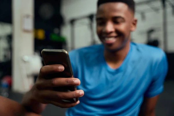 Homem afro-americano a olhar para o telemóvel. Feche os aplicativos de rolagem masculinos em seu telefone enquanto descansa no ginásio. Foto de alta qualidade — Fotografia de Stock