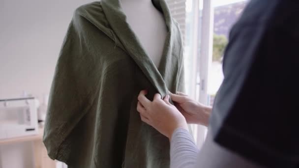 Кавказская студентка моды разрабатывает блузку для женщины, прикрепляющую булавки к манекену — стоковое видео