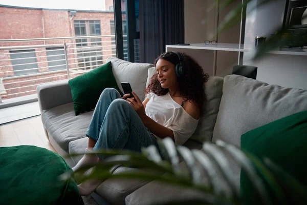 Змішана раса жіночий підліток з атро відпочиває на дивані з мобільним пристроєм — стокове фото