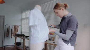 Beyaz kadın elbise tasarımcısı moda projesi için mankenlere bant yapıştırıyor. 