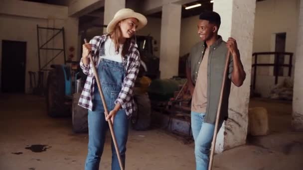 Masculino e feminino trabalhando agricultores varrendo sujo chão de galpão enquanto conversa — Vídeo de Stock