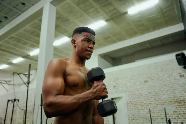 Hombre afroamericano sosteniendo pesas durante un entrenamiento intenso. Atleta masculino mirándose en el espejo del gimnasio mientras levanta pesas. Foto de alta calidad —  Fotos de Stock