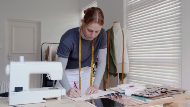 白人女性のドレスデザイナーは、ファッションスタジオでのドレスデザインのための測定値を書き留める — ストック動画
