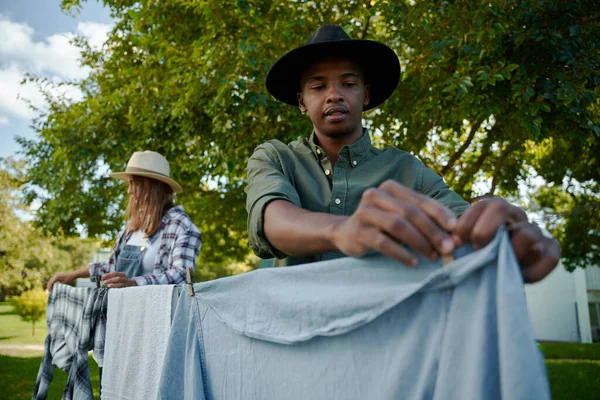 Mixed race male farmer hanging out dirty laundry outdoors — Stock Photo, Image