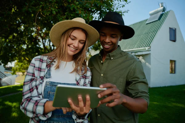 Raça mista agricultor masculino e feminino em pé junto por grama verde olhando para tablet digital — Fotografia de Stock