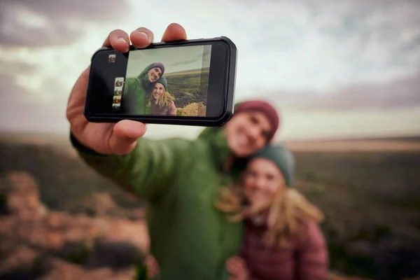 Primer plano de la mano masculina sosteniendo el teléfono inteligente tomando selfie con la novia mientras que en la colina de montaña después de la caminata — Foto de Stock