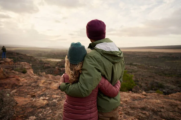 Vista trasera de la joven pareja enamorada abrazando mientras mira la hermosa naturaleza del paisaje después de caminar hasta el borde del acantilado de la montaña — Foto de Stock