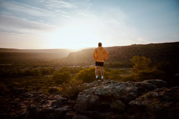 Achteraanzicht van de jonge atleet staan op de berg klif na ochtend lopen kijken naar de prachtige zonsopgang — Stockfoto