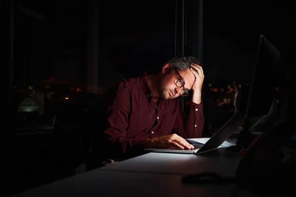 Втомився і стурбований бізнесмен на робочому місці в офісі, тримаючи голову на руках після роботи вночі на ноутбуці — стокове фото