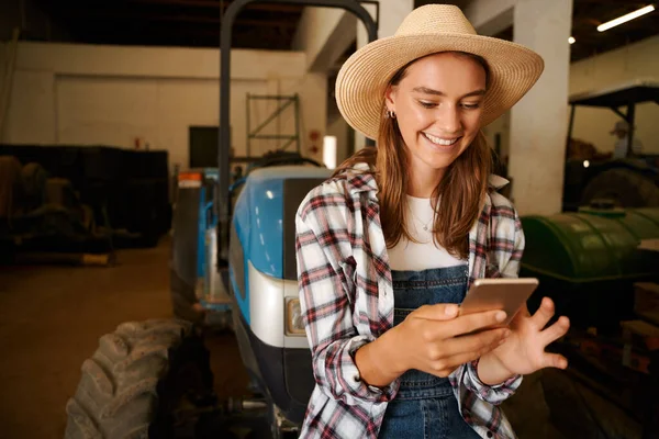 Femme agricultrice caucasienne textos sur dispositif cellulaire assis sur tracteur — Photo