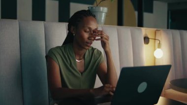 Modern ofis lobisinde dizüstü bilgisayarla çalışırken esnemekten yorgun düşmüş siyahi iş kadını.