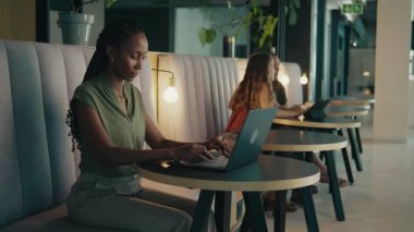 Modern ofis lobisinde dizüstü bilgisayar kullanan gülümseyen siyahi bir iş kadını.