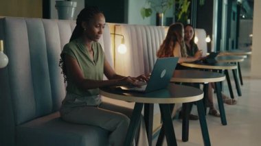 Modern ofis lobisinde dizüstü bilgisayarda çalışan gülümseyen siyahi bir iş kadını.