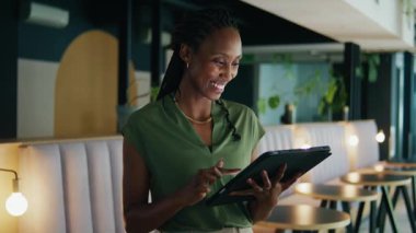 Modern ofis lobisinde tablet kullanarak akıllı, genç, siyah iş kadını gülümsüyor.