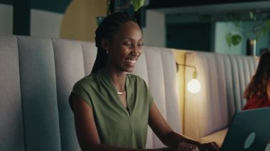 Modern aydınlanmış ofis lobisinde dizüstü bilgisayarda çalışan gülümseyen siyahi bir iş kadını.