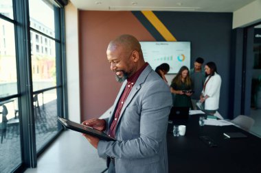 İş yerindeki modern toplantı odasında dijital tablet kullanan siyahi, olgun iş adamının yan görüntüsü