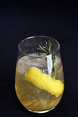 Böğürtlenli, buzlu ve cinle ferahlatıcı alkollü içecek, arka planda bulanık duran cam bardakta servis edilen limon kabuğu.