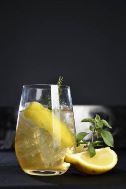 Böğürtlenli, buzlu ve cinle ferahlatıcı alkollü içecek, arka planda bulanık duran cam bardakta servis edilen limon kabuğu.