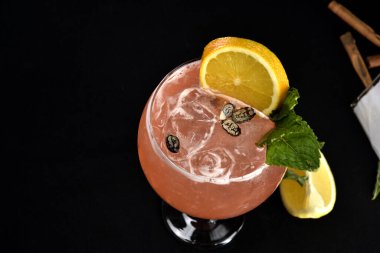 Böğürtlenli, buzlu ve cinle ferahlatıcı alkollü içecek, arka planda bulanık duran cam bardakta servis edilen limon kabuğu.