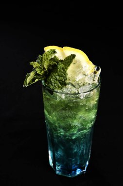 Böğürtlenli, buzlu ve cinle ferahlatıcı alkollü içecek, arka planda bulanık duran cam bardakta servis edilen limon kabuğu.