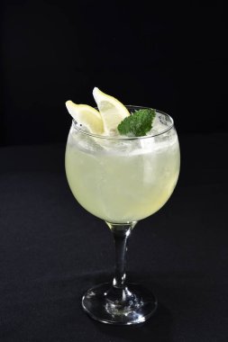 Böğürtlenli, buzlu ve cinle ferahlatıcı alkollü içecek, arka planda bulanık duran cam bardakta servis edilen limon kabuğu.