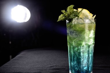 Böğürtlenli, buzlu ve cinle ferahlatıcı alkollü içecek, arka planda bulanık duran cam bardakta servis edilen limon kabuğu.