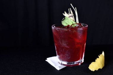 Böğürtlenli, buzlu ve cinli alkollü içecek, siyah arka planda cam bardakta servis edilen limon kabuğu.