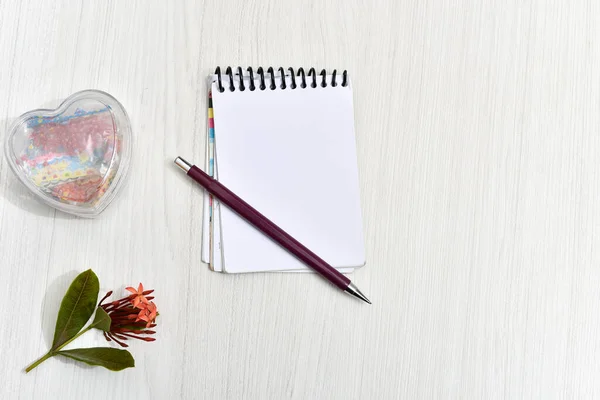 notepad with pencil, flower and heart on the table.