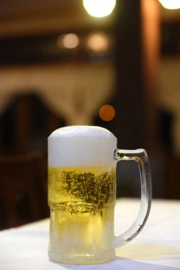 Enfes soğuk ve ferahlatıcı bira kupası bulanık arka planda masanın üstünde.