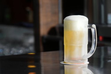 Enfes soğuk ve ferahlatıcı bira kupası bulanık arka planda masanın üstünde.