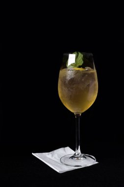 Böğürtlenli, buzlu ve cinle ferahlatıcı alkollü içecek, arka planda bulanık duran cam bardakta servis edilen limon kabuğu.