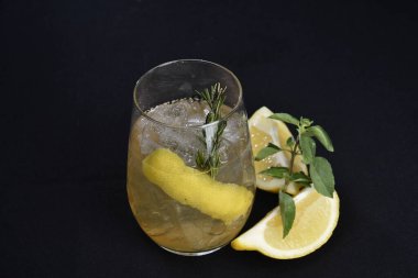 Böğürtlenli, buzlu ve cinle ferahlatıcı alkollü içecek, arka planda bulanık duran cam bardakta servis edilen limon kabuğu.