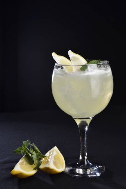 Böğürtlenli, buzlu ve cinle ferahlatıcı alkollü içecek, arka planda bulanık duran cam bardakta servis edilen limon kabuğu.