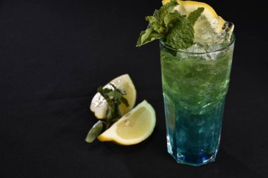 Böğürtlenli, buzlu ve cinle ferahlatıcı alkollü içecek, arka planda bulanık duran cam bardakta servis edilen limon kabuğu.