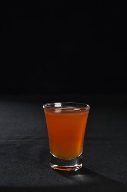 Böğürtlenli, buzlu ve cinle ferahlatıcı alkollü içecek, arka planda bulanık duran cam bardakta servis edilen limon kabuğu.