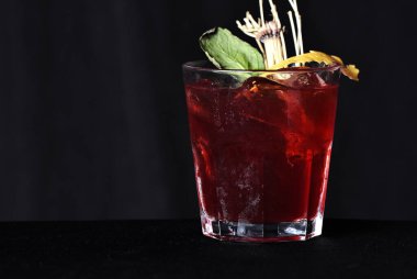 Böğürtlenli, buzlu ve cinli alkollü içecek, siyah arka planda cam bardakta servis edilen limon kabuğu.