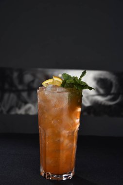 Böğürtlenli, buzlu ve cinle ferahlatıcı alkollü içecek, arka planda bulanık duran cam bardakta servis edilen limon kabuğu.