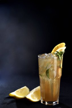 Böğürtlenli, buzlu ve cinle ferahlatıcı alkollü içecek, arka planda bulanık duran cam bardakta servis edilen limon kabuğu.