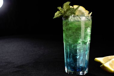 Böğürtlenli, buzlu ve cinle ferahlatıcı alkollü içecek, arka planda bulanık duran cam bardakta servis edilen limon kabuğu.